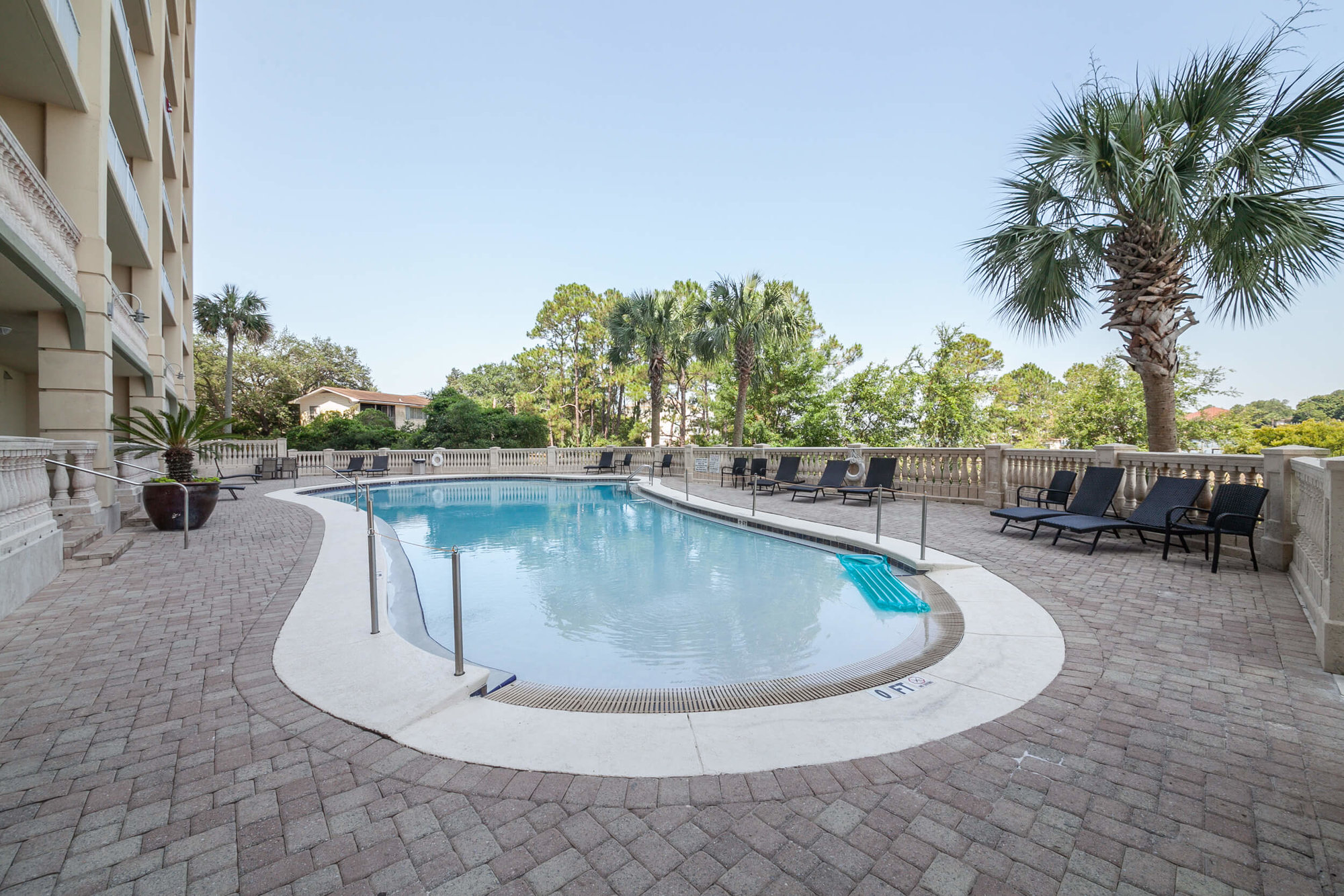 Zero entry pool surrounded by palm trees and large sundeck at Sailmaker's Place in Perdido Key